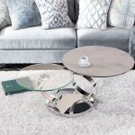 Photo d'ambiance présentant un salon avec une table basse. Les piètement sont en acier chromé avec un plateau en céramique effet béton noir.