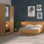 Photo d'ambiance d'une chambre avec un cadre de lit, une tête de lit avec étagère et lisseuse, une chiffonnier et une armoire. Le tout avec une finition en bois chêne sauvage. La collection s'inspire des vagues avec une teinte gris anthracite.